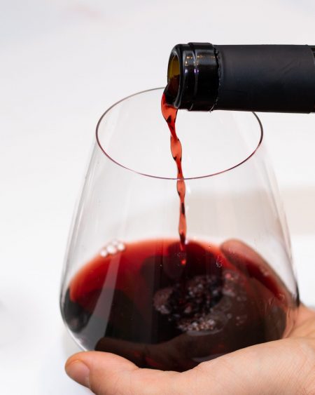 Red wine being poured into a large glass held in a hand