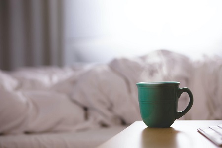 Green mug in front of messy bed